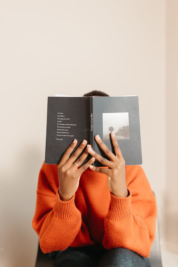 Person in orange sweater comfortably reading a book indoors.