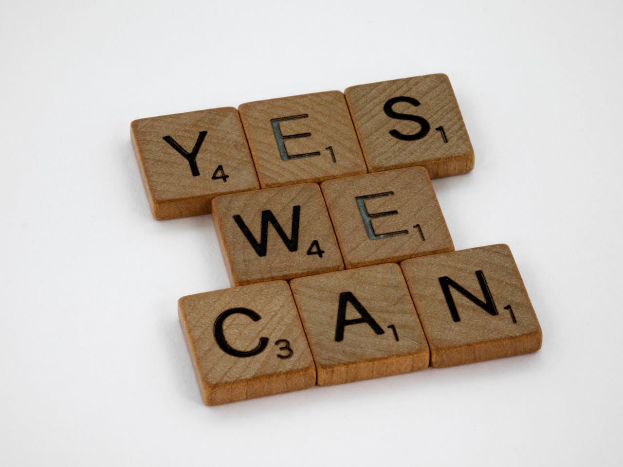 gallery-3 Wooden Scrabble tiles arranged to spell 'Yes We Can', emphasizing motivation on a white backdrop.