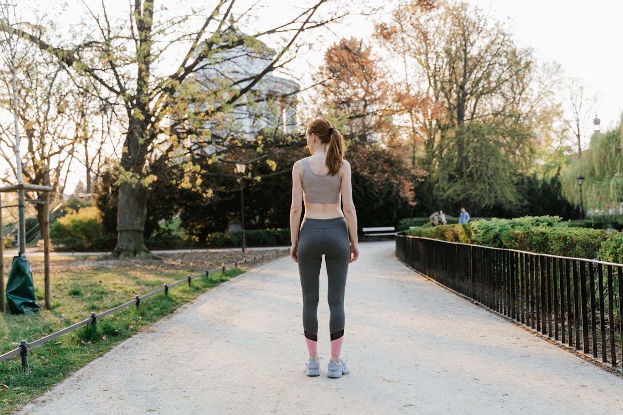 hero-img-02 A woman in activewear walks along a path in a sunny park, showcasing fitness in nature.